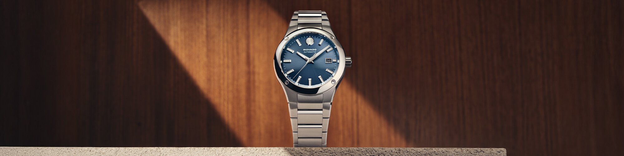 Museum Imperiale watch with silver bracelet and blue dial sitting on a stone ledge in front of a wooden wall.