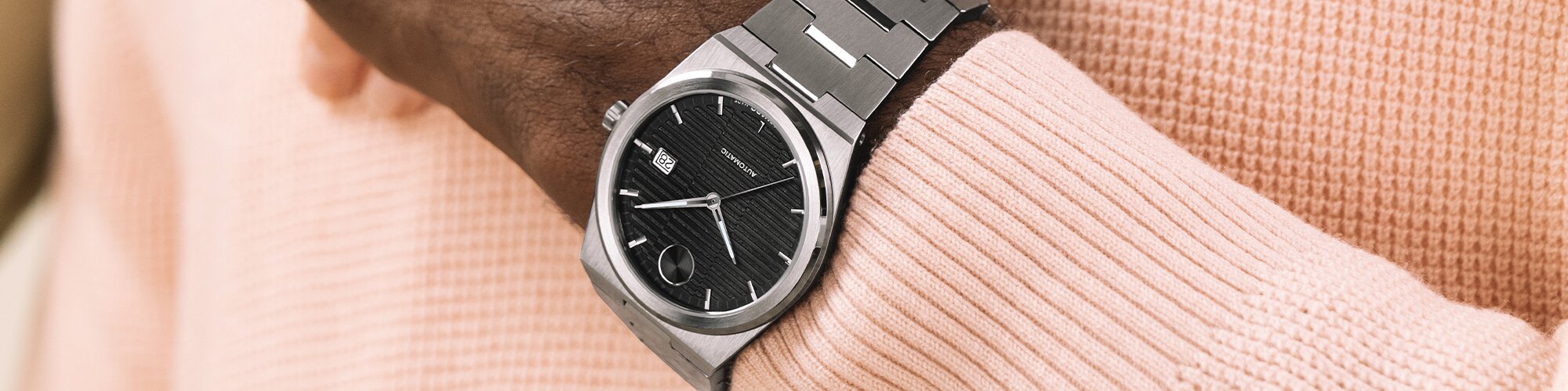 Man wearing a silver BOLD Quest Automatic bracelet watch with black dial holding a woman's hand that is wearing a gold tone BOLD Quest mini bracelet watch on her wrist