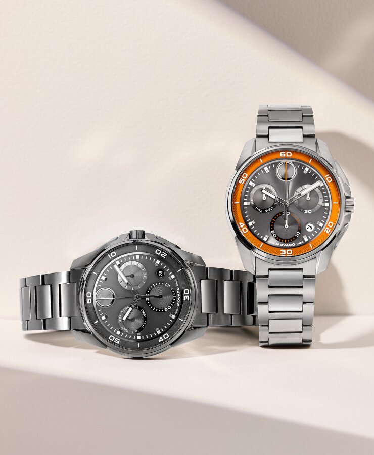 Grey plated BOLD Verso S Chronograph bracelet watch laying next to a BOLD Verso S Chronograph watch with stainless steel bracelet and grey dial with orange minute track.