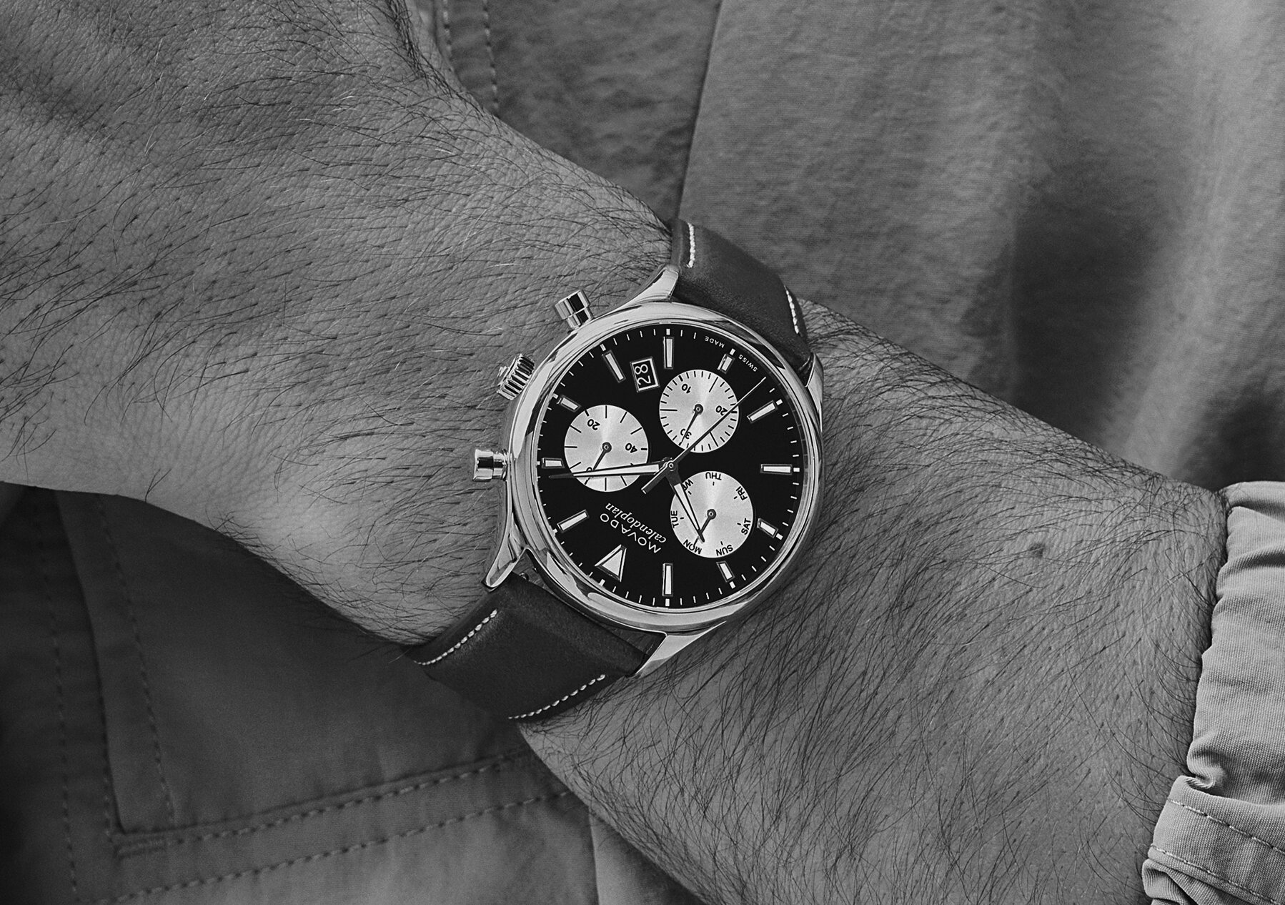 Man in a green jacket wearing the Heritage Calendoplan watch with brown strap and blue chronograph dial.