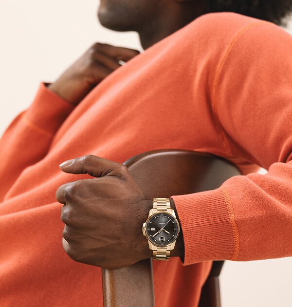 Man in an orange sweater wearing the BOLD Verso Automatic watch with gold tone bracelet and grey dial on his wrist.