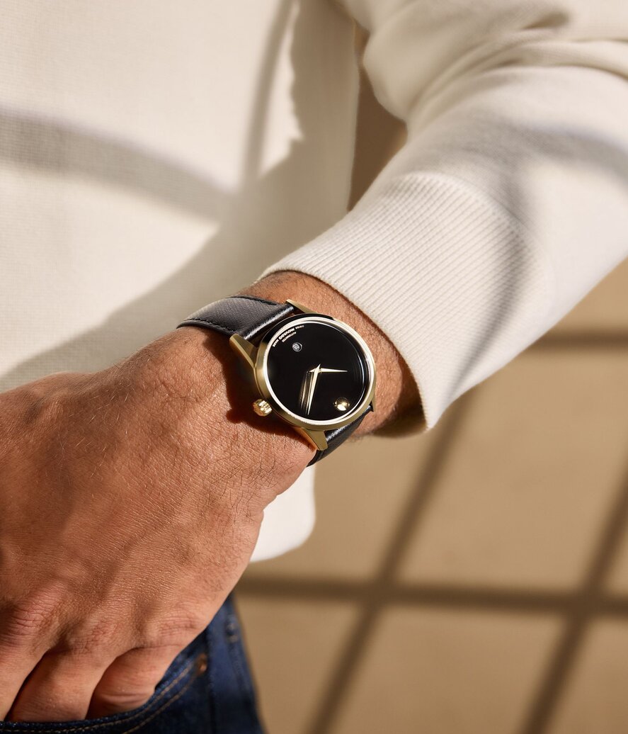 Man in a white sweater wearing the black Museum Classic watch with leather strap and gold accents.