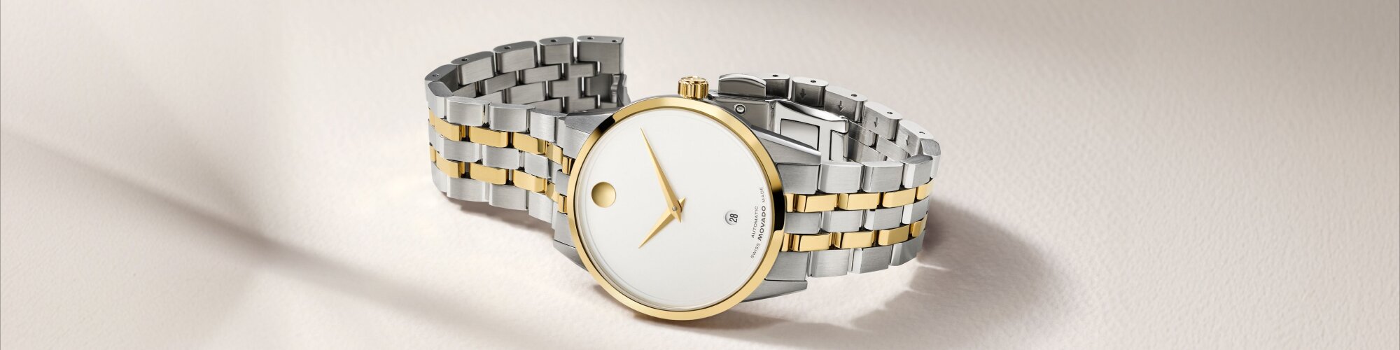 Museum Classic Automatic watch with two tone bracelet and white dial with gold accents laying on its side.