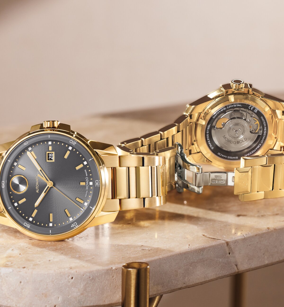 Front of a BOLD Verso Automatic watch with grey dial and gold tone bracelet laying in front of the back of the BOLD Verso Automatic watch with a caseback that displays the automatic movement