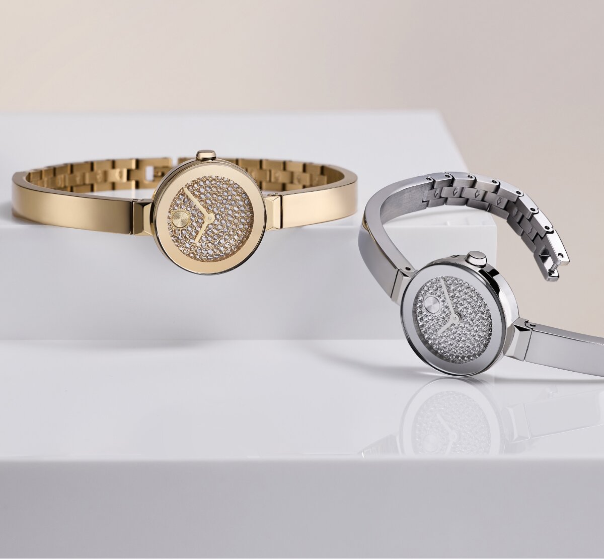 Stainless Steel BOLD Bangle Mini watch with crystal dial laying in front of a gold tone BOLD Bangle Mini watch with crystal dial.