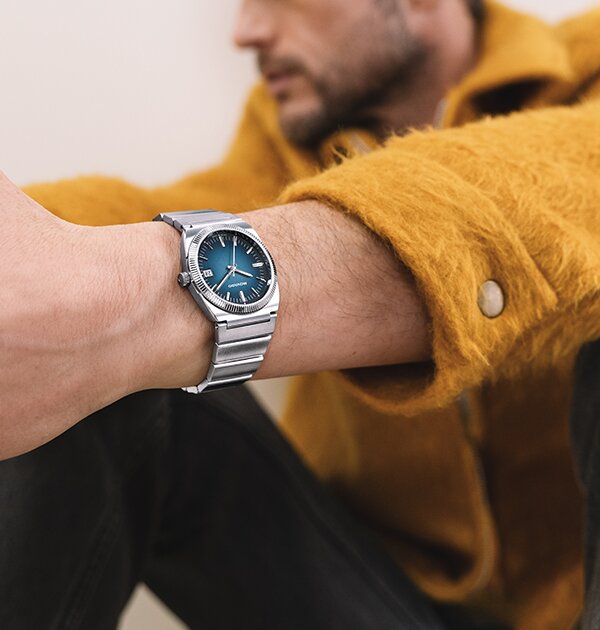 Man in an orange jacket wearing a Movado Heritage Series Ondpolan watch with silver bracelet and blue dial