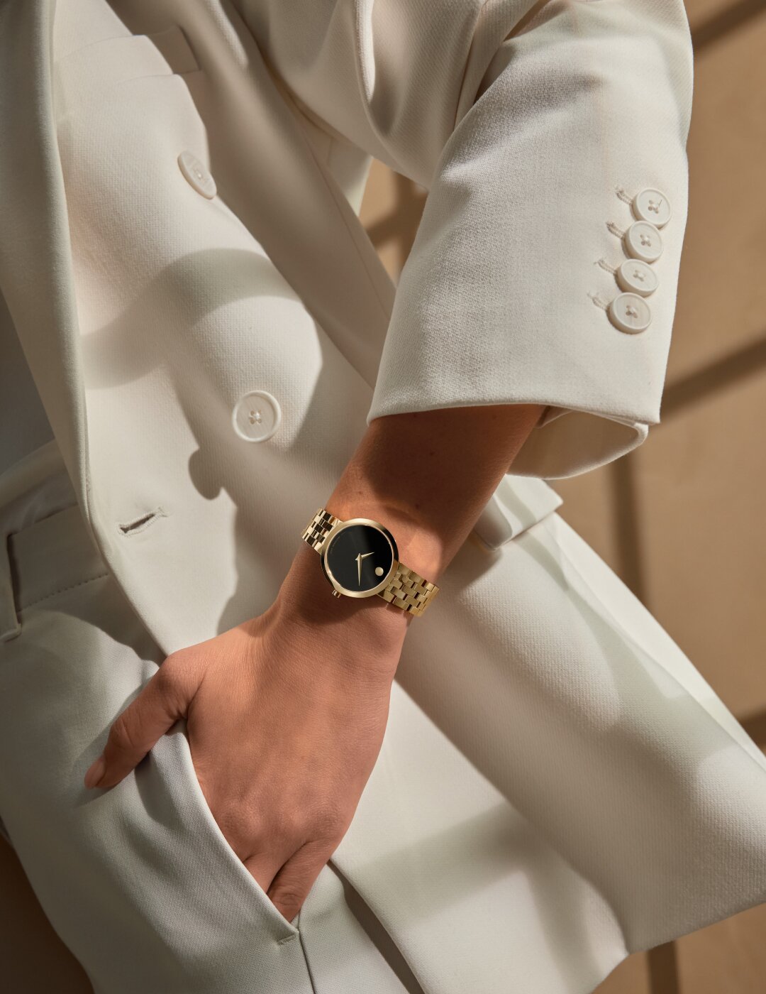 Woman in a white suite wearing the Museum Classic watch with gold tone bracelet and black dial.