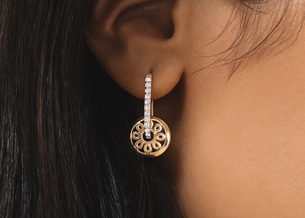 Gold tone fleur charm earring on a women's ear