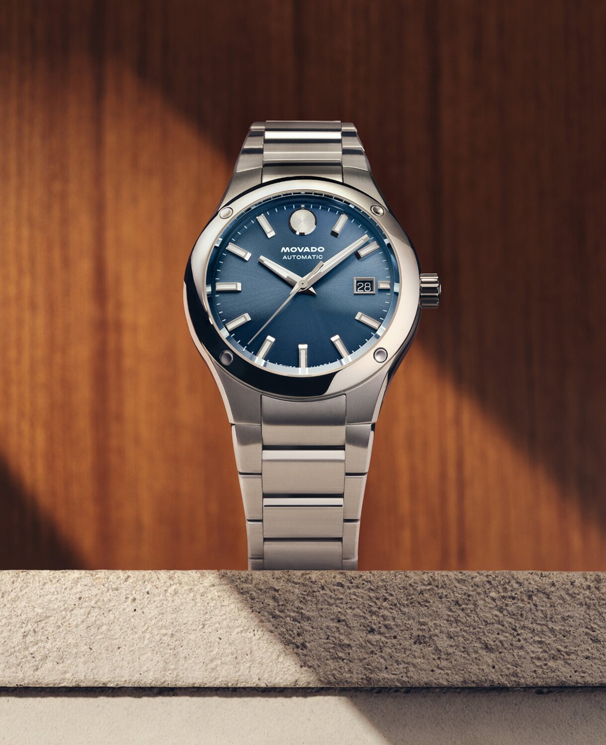 Museum Imperiale watch with silver bracelet and blue dial sitting on stone in front of a wooden panel.