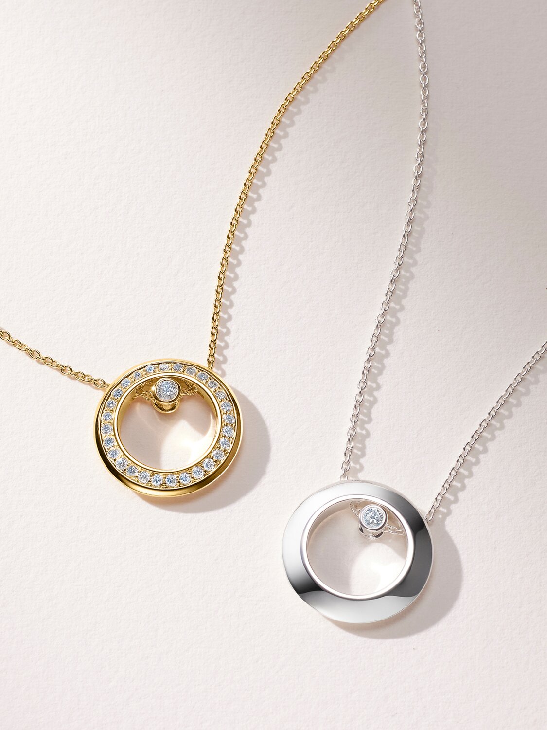 Gold tone necklace with lab grown diamonds next to a silver necklace with one lab grown diamond.