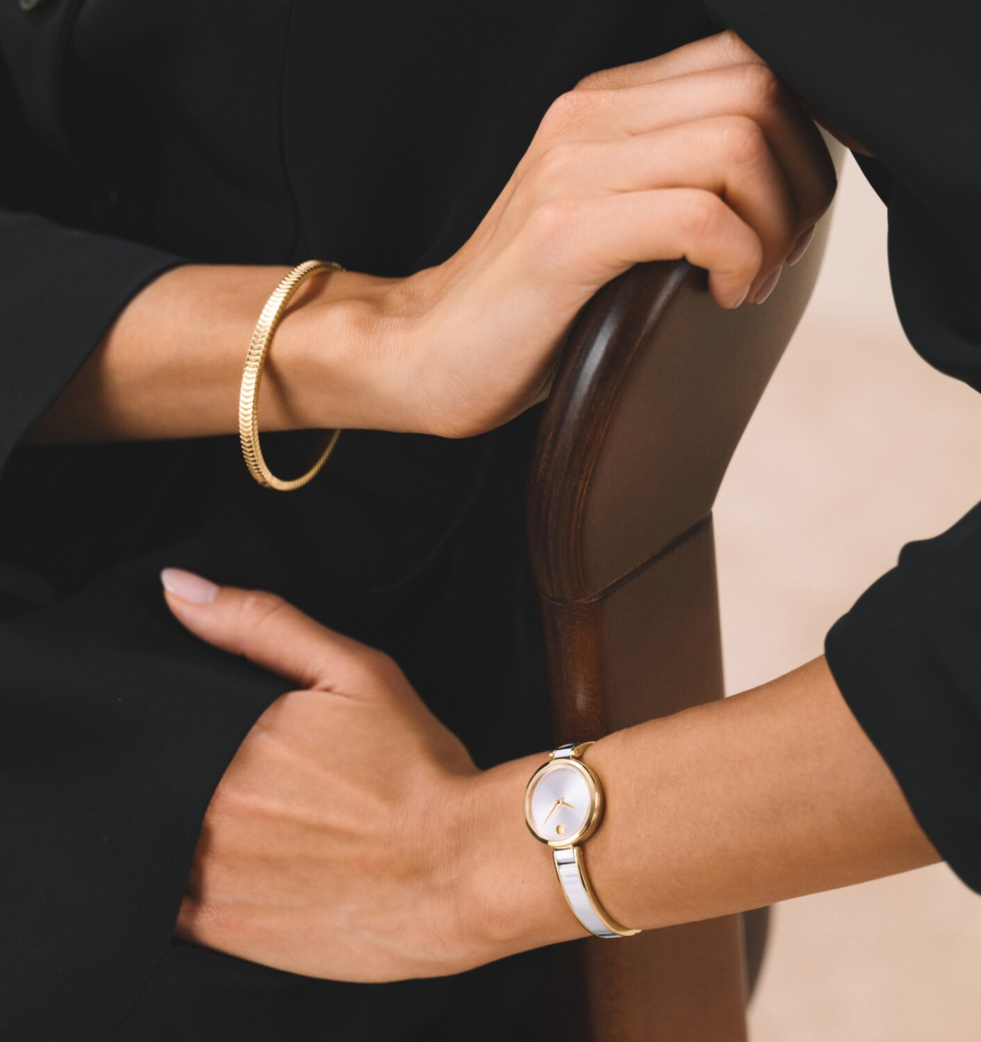 Woman in a black shirt and black pants wearing a gold bracelet and the silver Moda bangle watch with gold accents