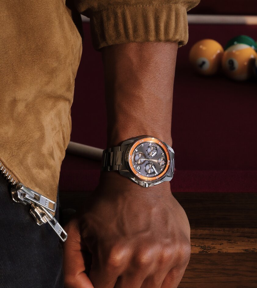 Man holding a steering wheel wearing the BOLD Verso S watch with black strap, grey dial and red hour track.