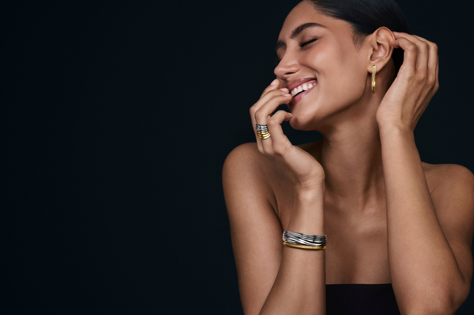 Woman wearing silver and gold tone Curve earrings, rings and bangles.