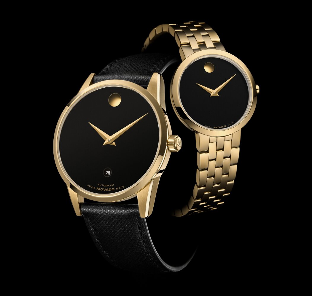 Black Museum Classic Automatic watch with leather strap and gold accents in front of a women's Museum Classic watch with gold tone bracelet and black dial. 