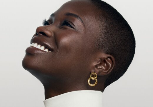 Woman smiling wearing gold tone Curve double hoop earrings.