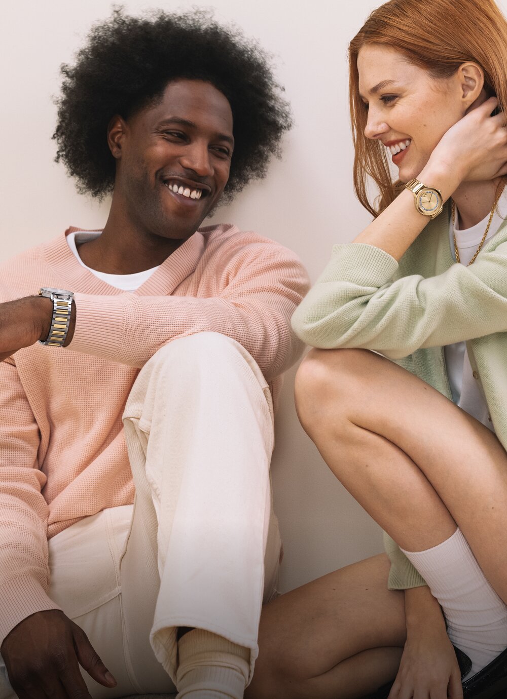 Man sitting down wearing a two tone BOLD Evolution 2.0 watch next to a woman kneeling wearing a gold tone BOLD Evolution 2.0 watch with baguette crystals.