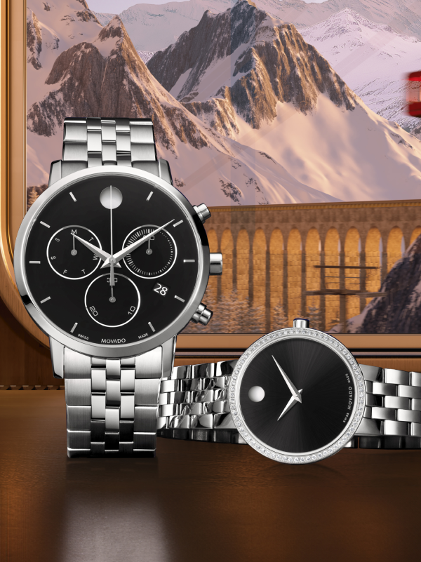 Women's silver museum classic watch with diamonds laying down next to a Silver Men's Museum Classic chronograph watch sitting up with Swiss mountains in the background