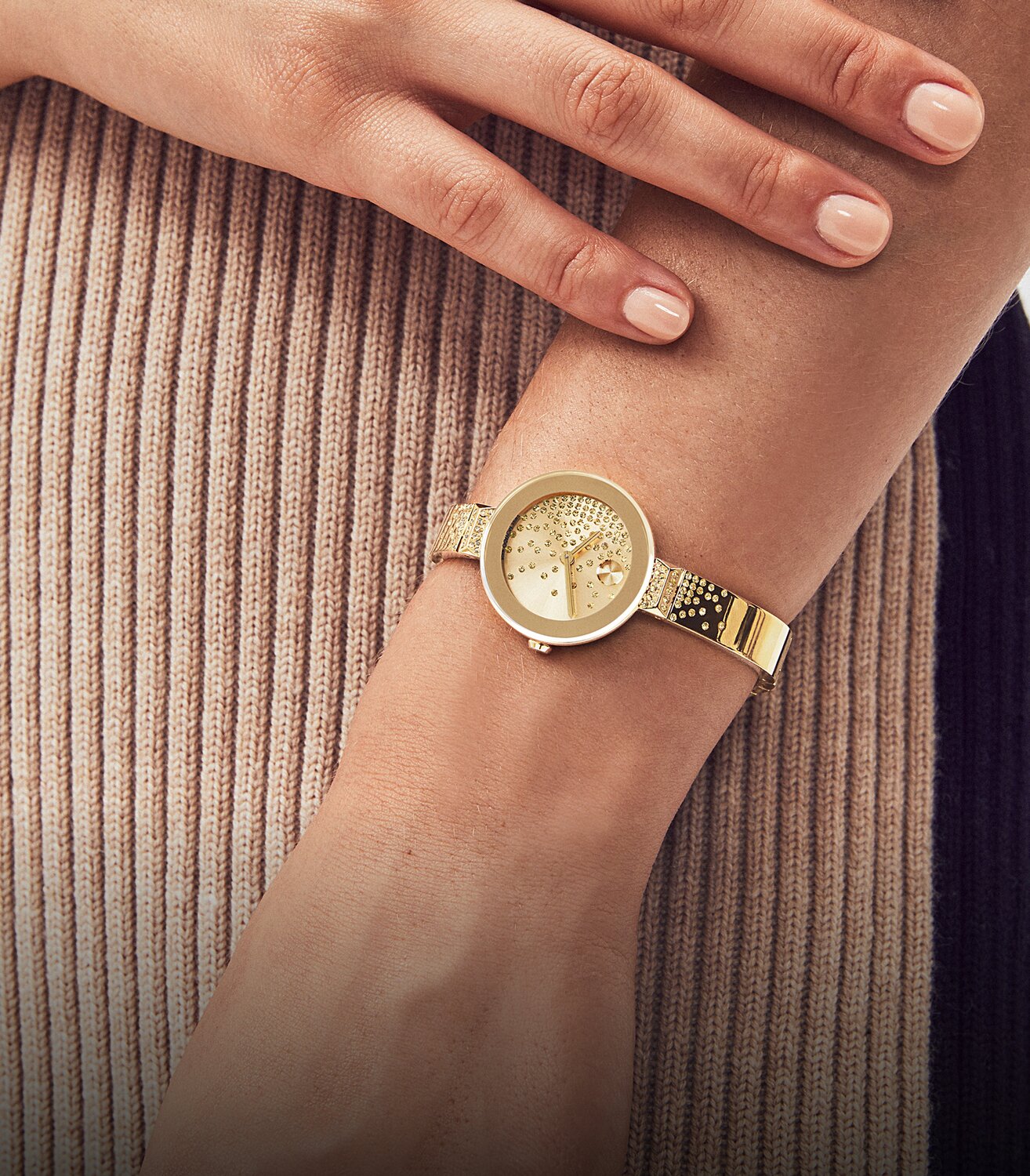 Woman in a brown sweater wearing the gold tone BOLD Bangle watch with cascading crystals on the dial and bracelet.
