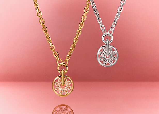 Gold tone Movado Fleur necklace featuring lab grown diamonds next to a silver Movado Fleur necklace  hanging in front of a red background 