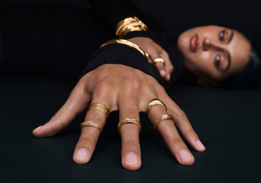 Woman laying down with her hand in the foreground wearing 4 gold tone Curve rings.