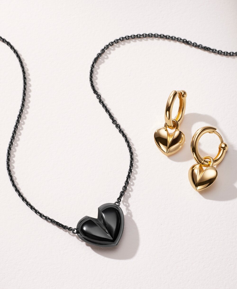 Women's black plated heart necklace next to gold tone hoop earrings with heart charm.