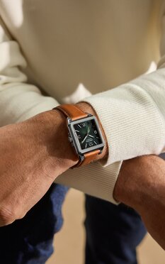 Man in a white sweater wearing the Heritage 1917 watch with brown leather strap and green square dial.