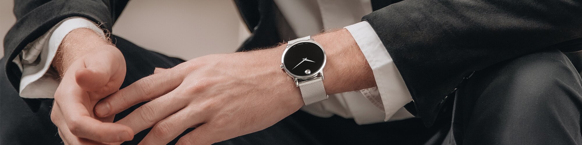 Man in a suit wearing a Museum classic watch with silver mesh strap and black dial