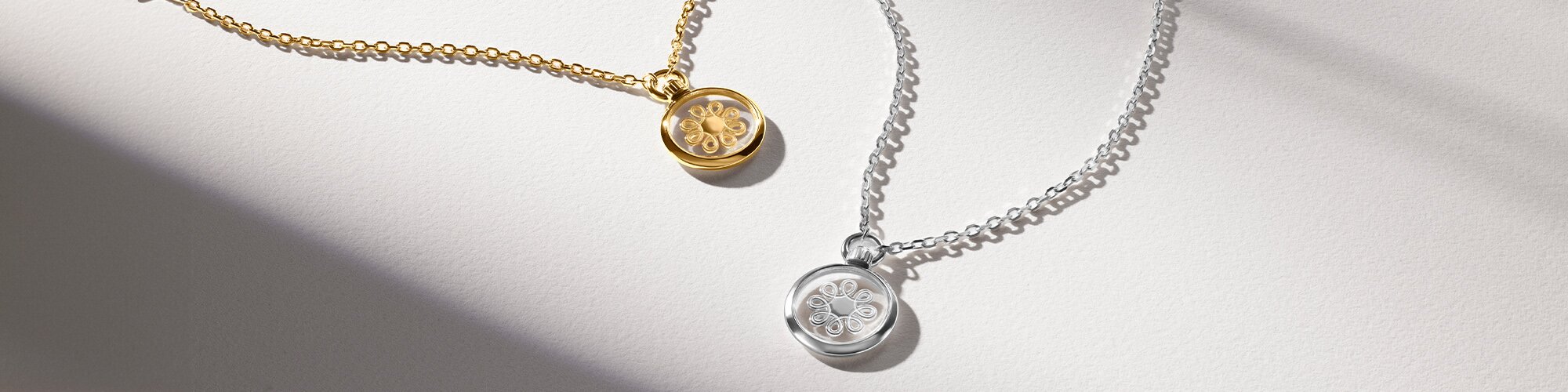 Gold tone necklace with fleur charm next to silver fleur charm necklace