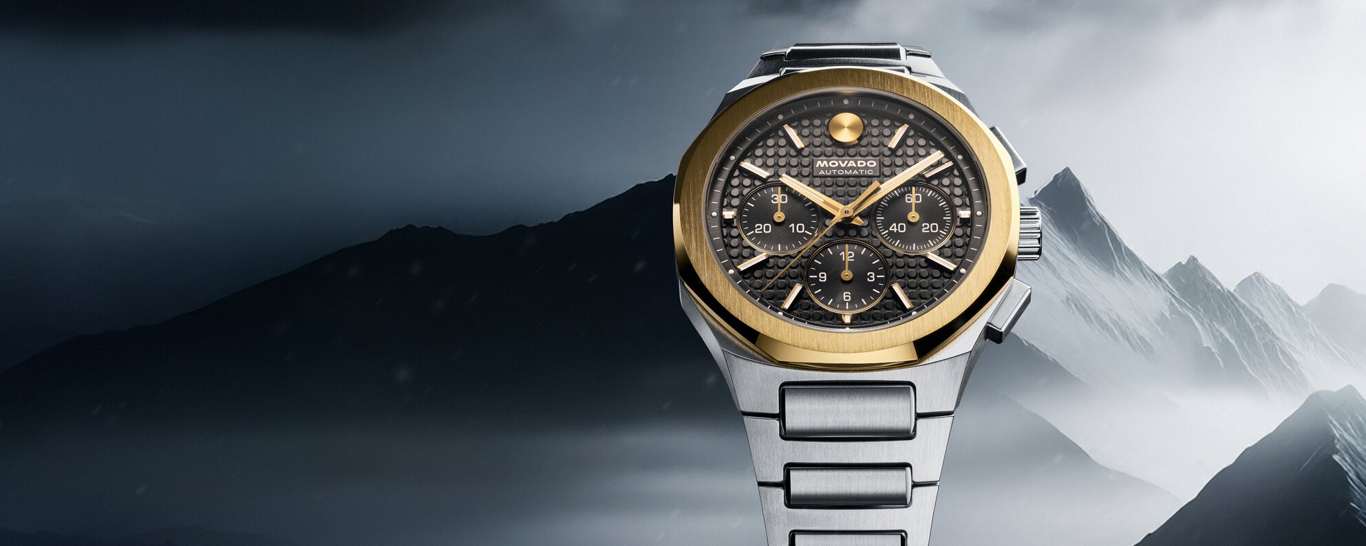 Two Tone Alta Centurion bracelet watch with 18K Gold Bezel in front of mountains.