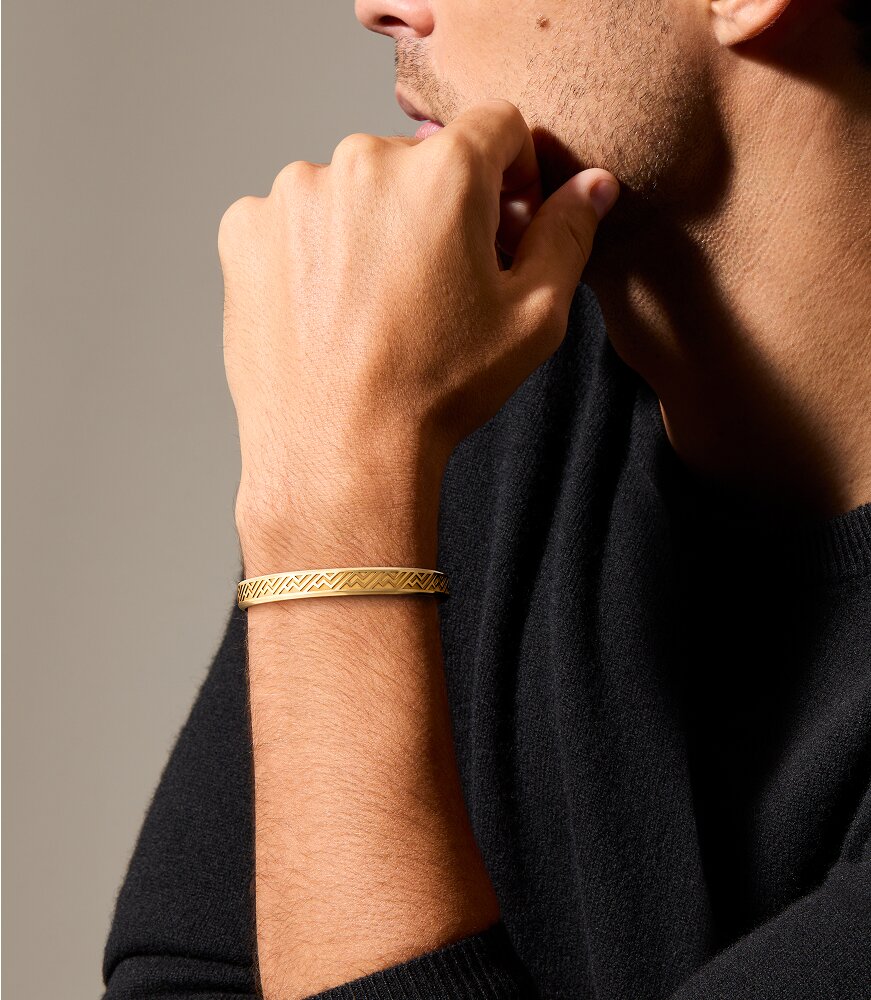 Man in a black sweater, leaning on his hand, wearing the gold plated cuff bracelet.