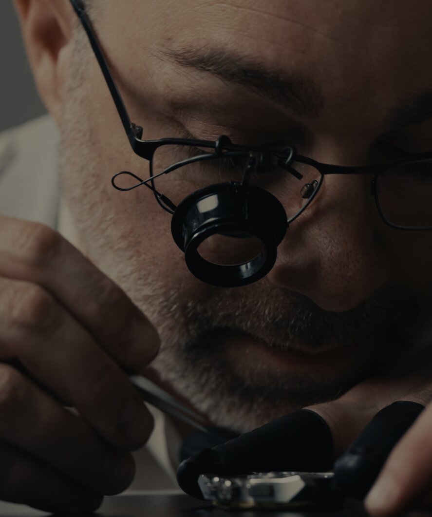 Man looking into a magnifying glass, assembling an automatic movement by hand.
