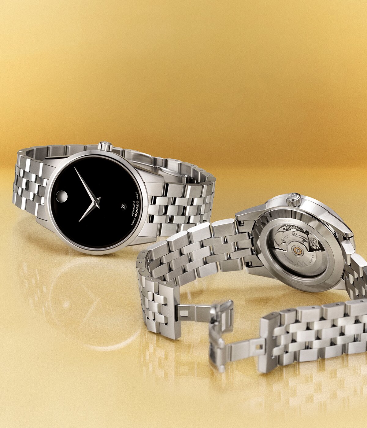 Front of a Museum Classic Automatic watch with silver bracelet and black dial laying next to the back of the Museum Classic Automatic watch featuring an exposed automatic movement in the caseback.