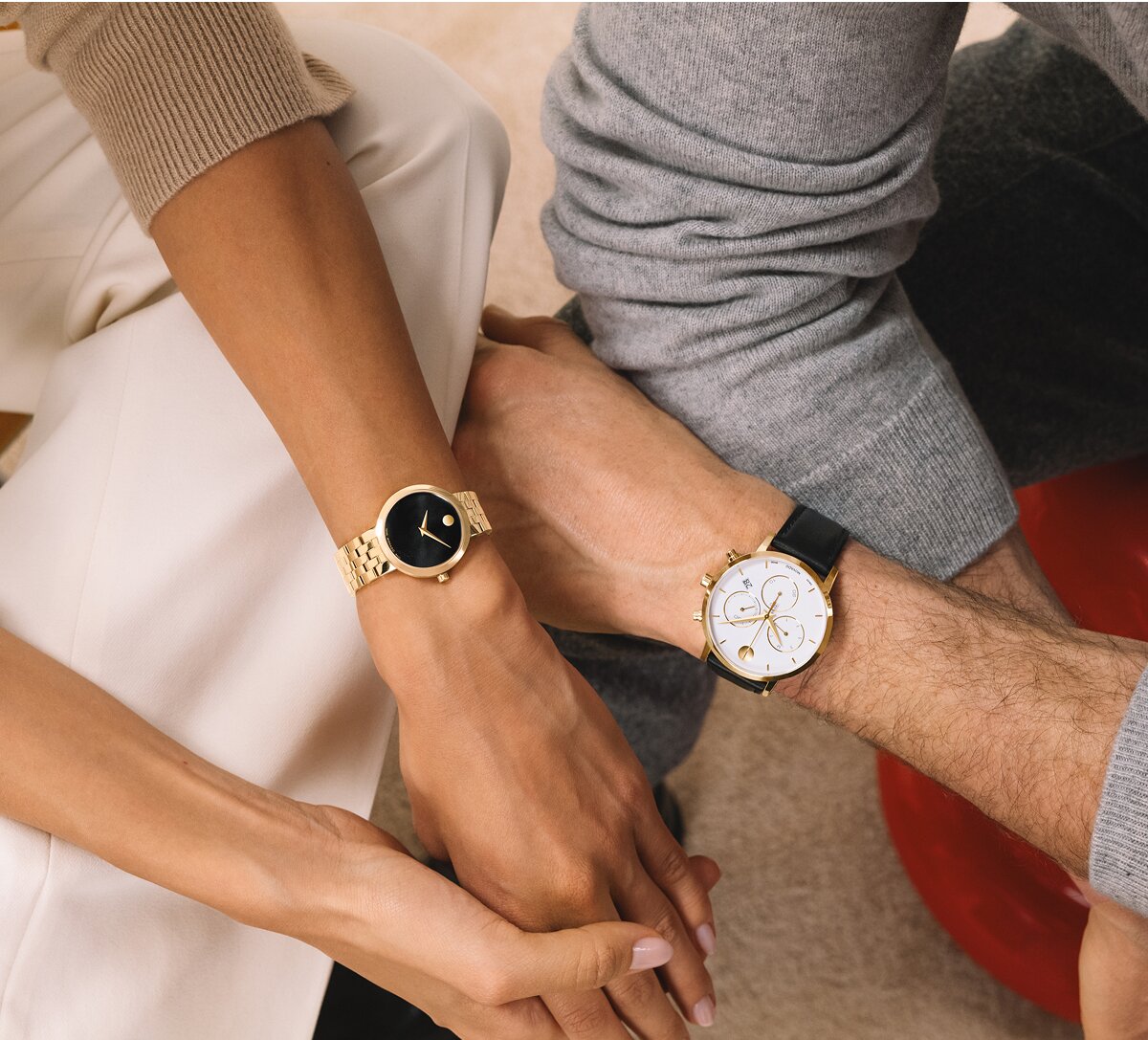 Woman wearing a gold tone Museum Classic bracelet watch with black dial sitting next to a man wearing a Museum Classic watch with a black strap and white Chronograph dial. 