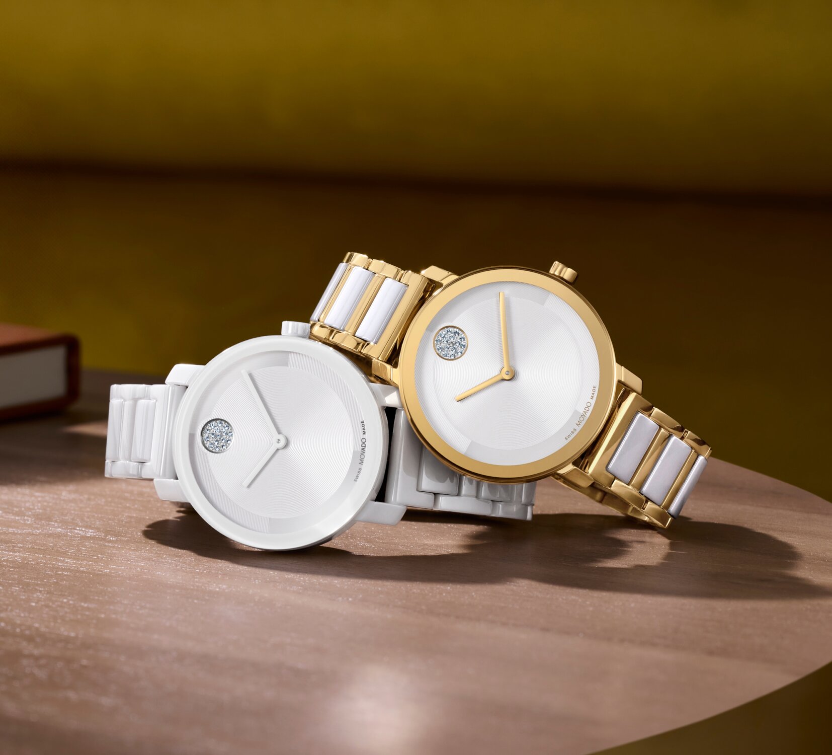 All white ceramic BOLD Evolution 2.0 watch laying underneath a gold BOLD Evolution 2.0 watch with white ceramic links on a desk