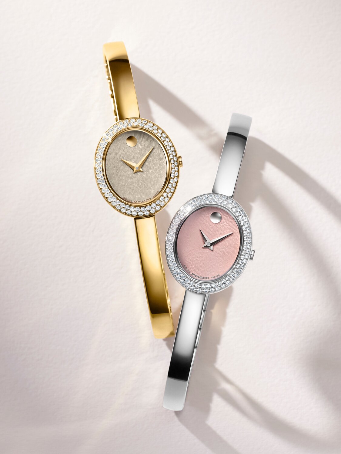 Gold tone bangle watch next to silver bangle watch with pink oval dial.