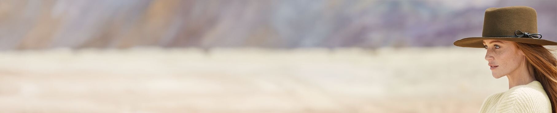 Woman wearing an olive color flat felt hat looks toward the left side of the screen.