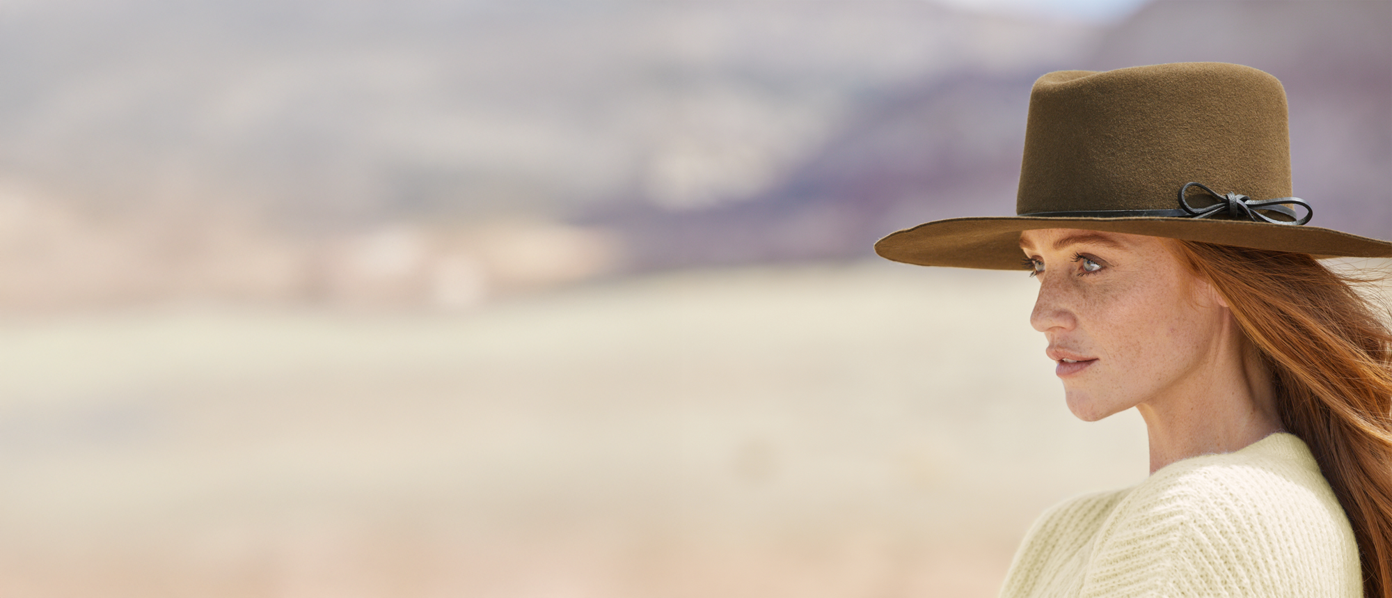 Woman wearing an olive color flat felt hat looks toward the left side of the screen.