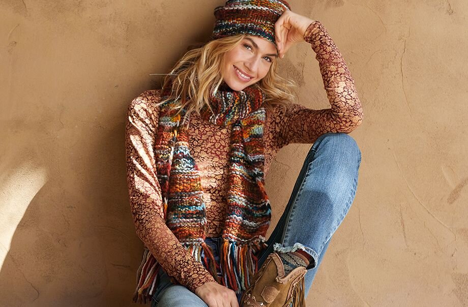 Woman wearing a knit hat, scarf and sweater from Peruvian Connection poses against a tan wall.