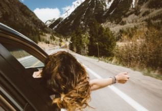 Cross Country color photo of woman with head and arm out of vehicle window.            