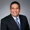 Cross Country color portrait photo of John A. Martins, President and Chief Executive Officer. John is a light-skinned man with dark, short hair. He is wearing a dark-colored suit coat over a light-colored shirt and a light blue necktie. 