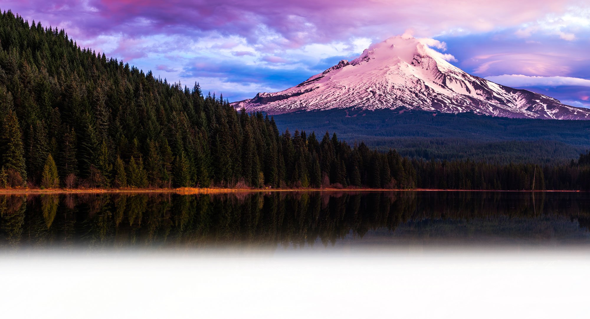 Cross Country Healthcare color photo of snow-covered mountain and pine trees around a lake.                                  