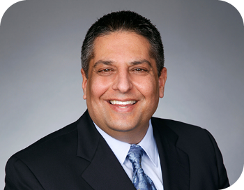Cross Country clickable color portrait photo of John A. Martins, President and Chief Executive Officer. John is a lighter skinned man with short-cropped dark hair. He is wearing a dark suit jacket over a white button-up shirt with a light blue silk necktie.                                                                              