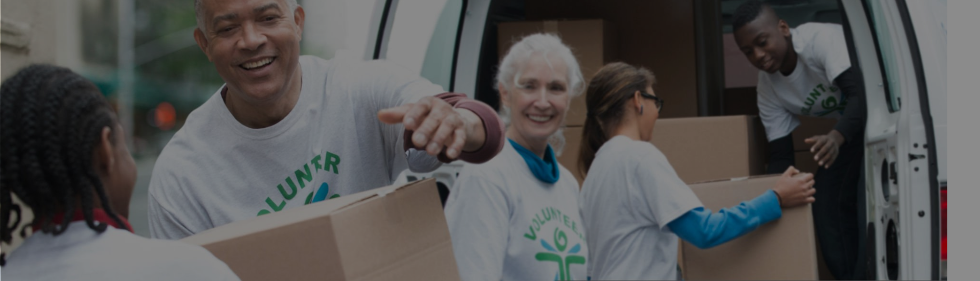 Cross Country header color photo showing group of four volunteers shuffling cardboard boxes.          