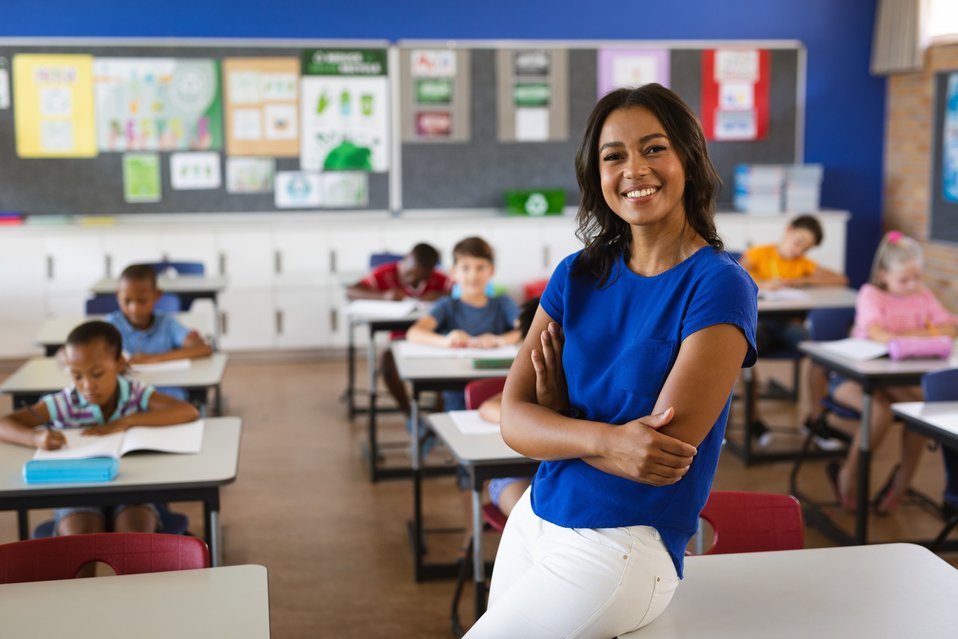 Cross Country color photo of female in classroom wearing blue shirt with arms akimbo.                    