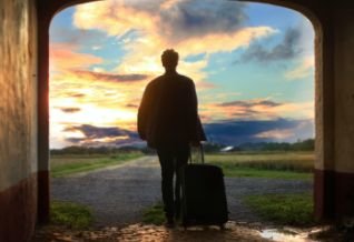 Cross Country color photo of person with rolling luggage silhouetted against a sunset.          