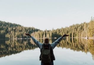 Cross Country color photo of person with arms outstretched to lake and trees.          