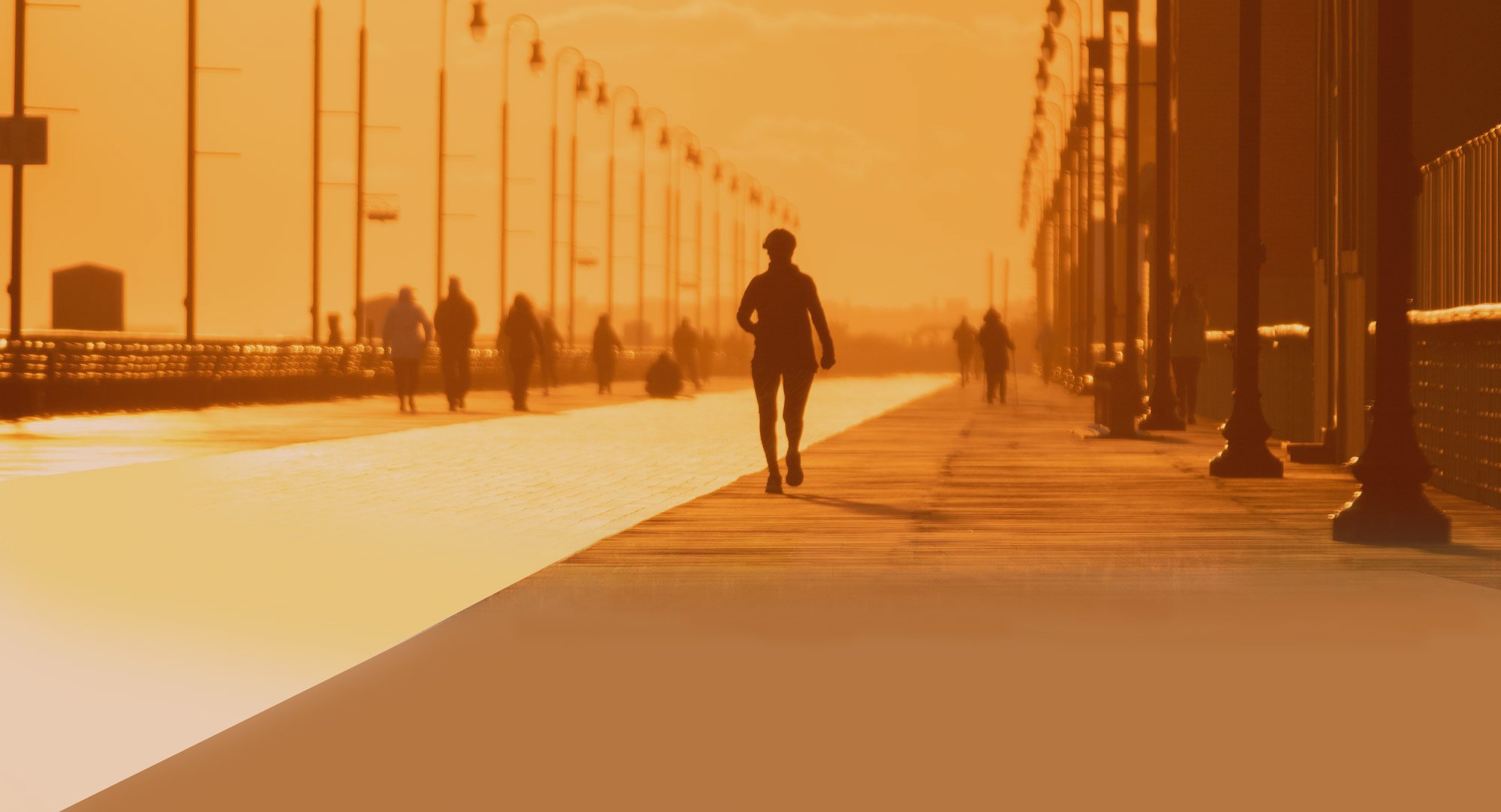 Cross Country Healthcare color photo of people on a boardwalk silhouetted against a yellow background. 