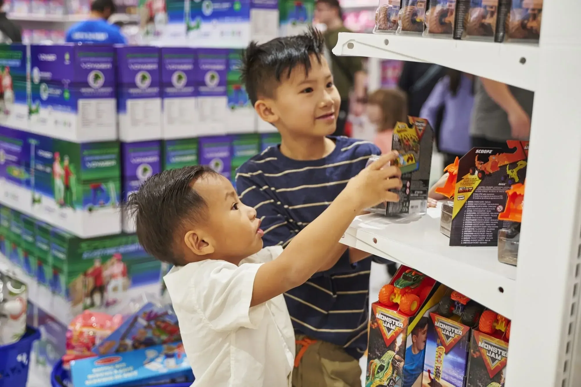 Two young boys reaching for toy boxes together on a bright shelf at Go! Toys and Games