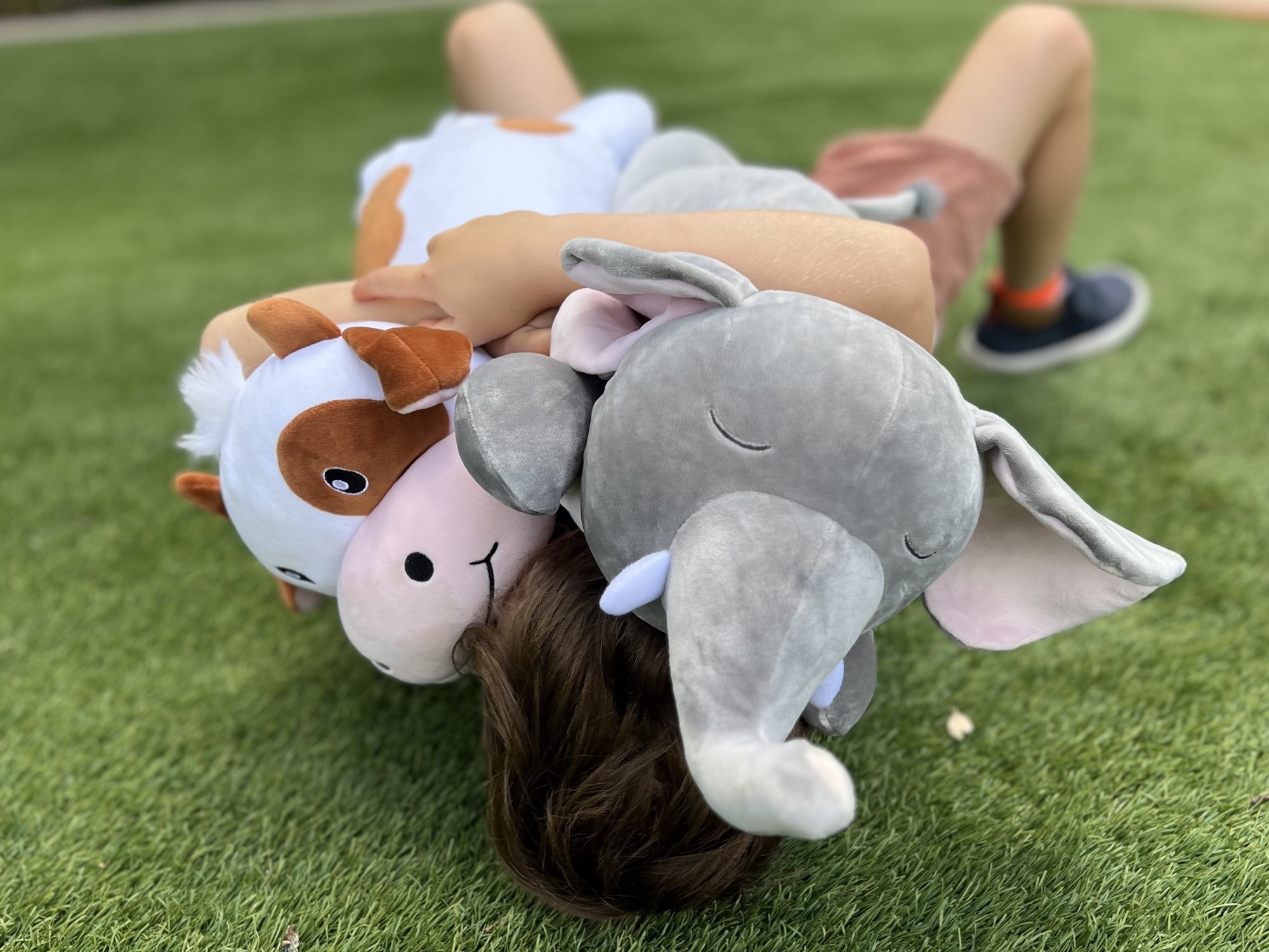 A child lying in the grass completely surrounded by soft Snoozimal plush friends