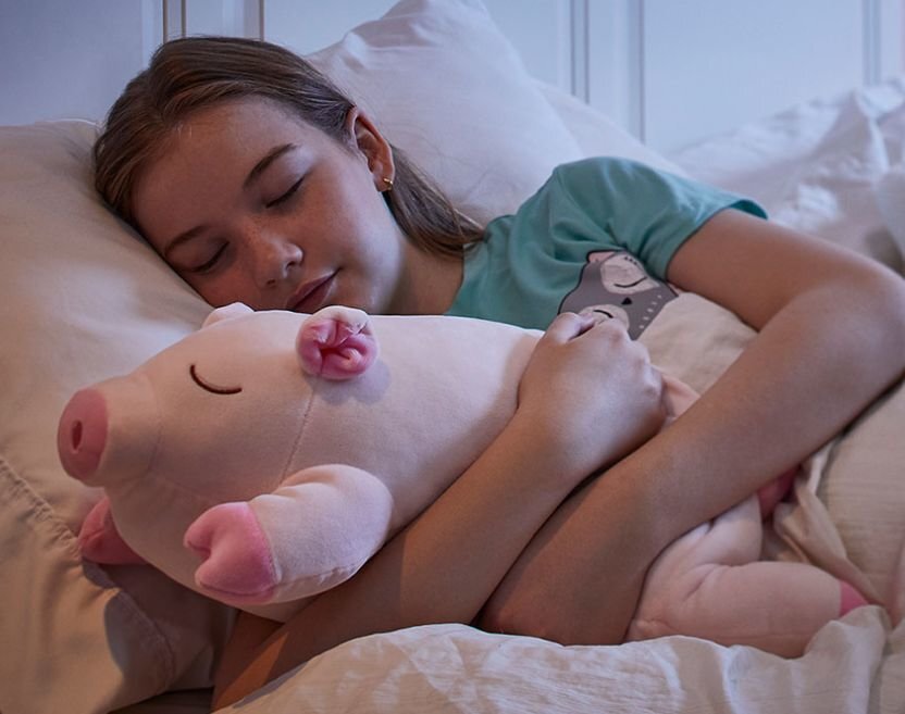 A girl sleeping peacefully in bed hugging her Snoozimal plush